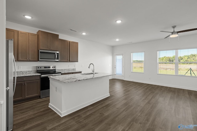 kitchen featuring light stone counters, dark hardwood / wood-style floors, a kitchen island with sink, appliances with stainless steel finishes, and sink