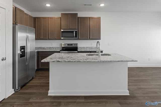 kitchen with a kitchen island with sink, stainless steel appliances, light stone countertops, dark hardwood / wood-style floors, and sink