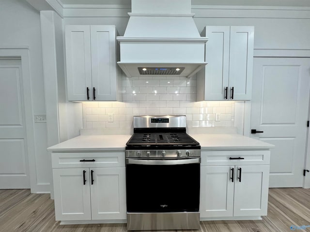 kitchen featuring custom range hood, light wood-type flooring, stainless steel gas range, and white cabinetry