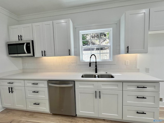 kitchen featuring light hardwood / wood-style floors, sink, white cabinets, decorative backsplash, and appliances with stainless steel finishes