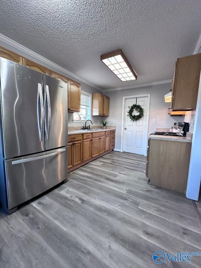 kitchen with brown cabinetry, wood finished floors, freestanding refrigerator, ornamental molding, and light countertops