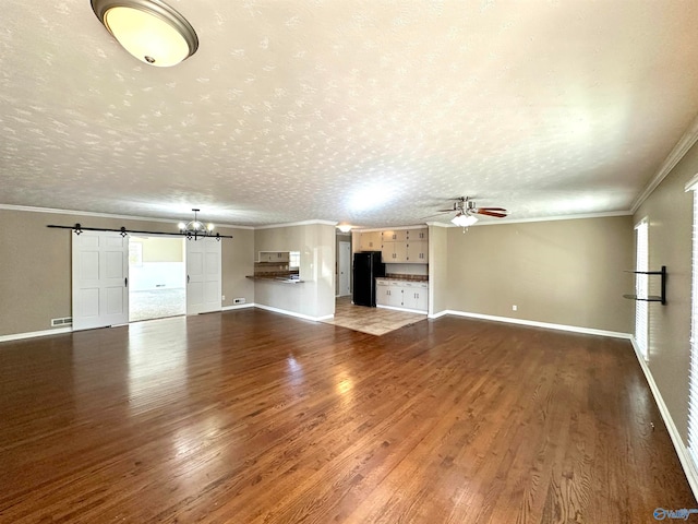 unfurnished living room with crown molding, a barn door, a textured ceiling, ceiling fan with notable chandelier, and dark hardwood / wood-style flooring