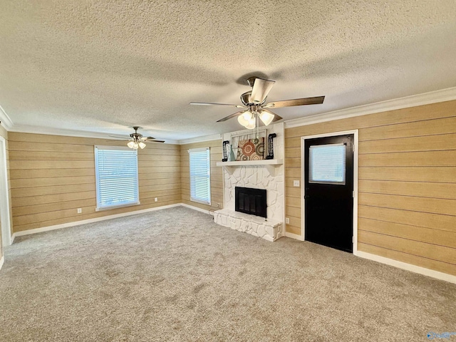 unfurnished living room with ceiling fan, wood walls, a textured ceiling, and ornamental molding