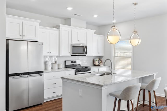 kitchen featuring a center island with sink, appliances with stainless steel finishes, dark wood-type flooring, and backsplash