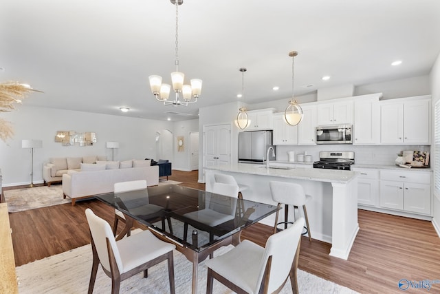 dining space featuring arched walkways, recessed lighting, a notable chandelier, baseboards, and light wood-style floors