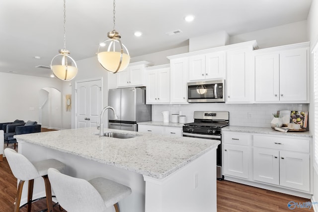 kitchen featuring arched walkways, appliances with stainless steel finishes, an island with sink, and white cabinets