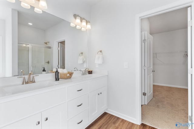 bathroom featuring double sink vanity, a shower with shower door, and wood-type flooring