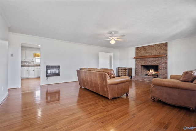 living room featuring light wood-type flooring, a fireplace, a ceiling fan, and ornamental molding