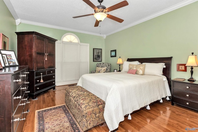 bedroom with a textured ceiling, wood-type flooring, ornamental molding, and ceiling fan