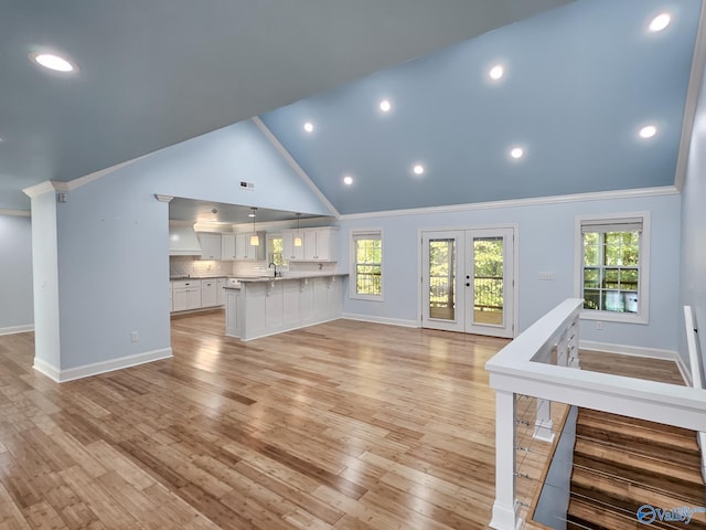 unfurnished living room with light wood-type flooring, high vaulted ceiling, crown molding, and sink