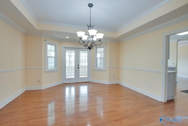 empty room featuring a tray ceiling, french doors, baseboards, and light wood-style floors