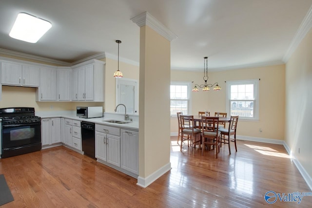 kitchen with light countertops, ornamental molding, light wood-style flooring, black appliances, and a sink