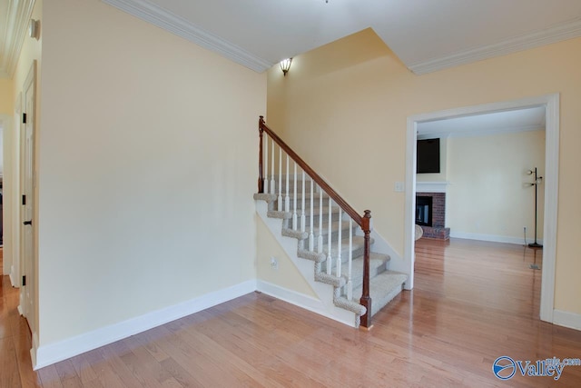 stairs featuring baseboards, wood finished floors, a brick fireplace, and ornamental molding