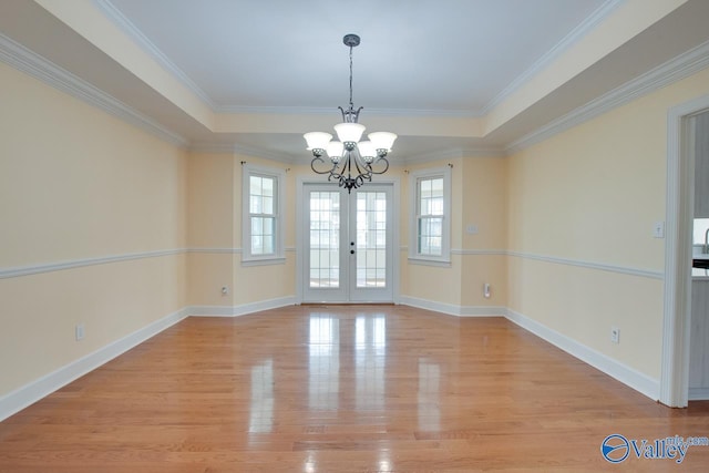 unfurnished room with an inviting chandelier, a raised ceiling, baseboards, and light wood finished floors