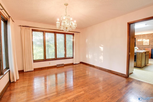 unfurnished dining area with a notable chandelier, light hardwood / wood-style floors, and a textured ceiling