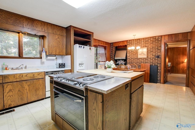 kitchen featuring sink, white appliances, hanging light fixtures, wooden walls, and a chandelier