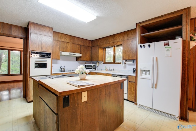 kitchen featuring sink, white appliances, a center island, and a textured ceiling