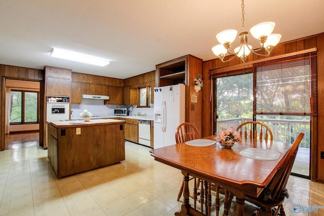 kitchen featuring pendant lighting, white appliances, a kitchen island, and wood walls