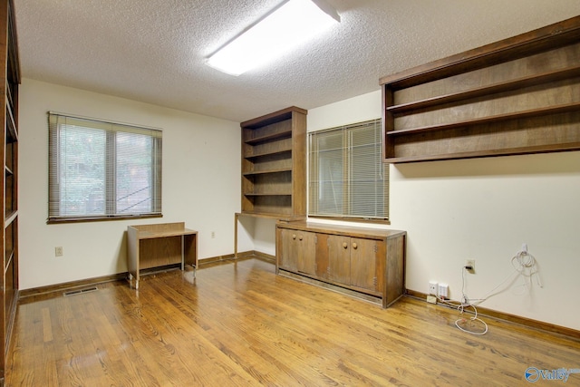 unfurnished office featuring built in desk, light hardwood / wood-style floors, and a textured ceiling