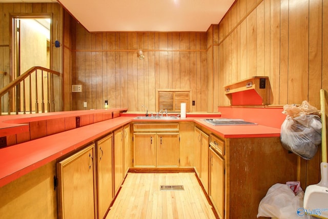 kitchen featuring stainless steel gas stovetop, wooden walls, sink, and light hardwood / wood-style flooring