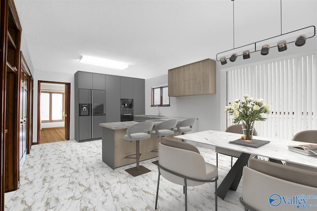 kitchen with sink, multiple ovens, built in refrigerator, a textured ceiling, and a kitchen breakfast bar