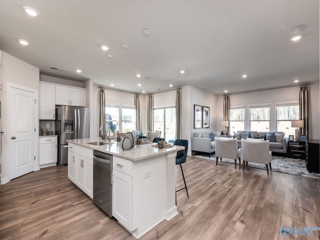 kitchen featuring stainless steel appliances, a kitchen island with sink, open floor plan, and white cabinets