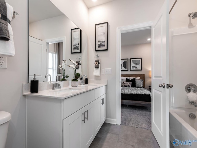 ensuite bathroom with toilet, a sink, washtub / shower combination, double vanity, and baseboards