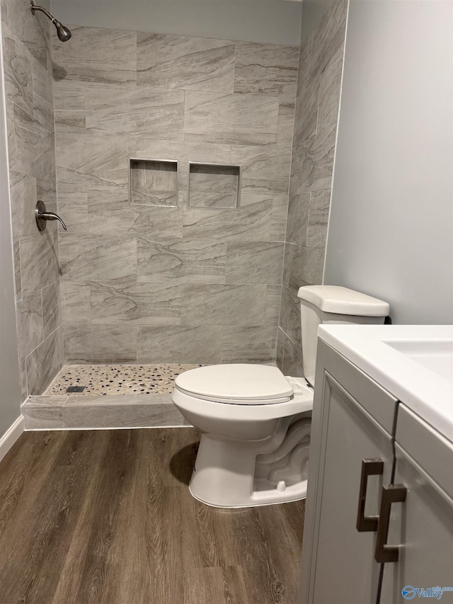full bathroom with wood finished floors, vanity, a tile shower, and toilet
