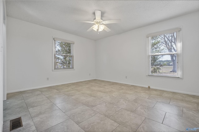 spare room featuring visible vents, baseboards, a textured ceiling, and a ceiling fan