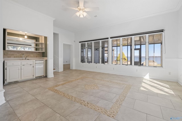 unfurnished living room with a sink, crown molding, light tile patterned floors, baseboards, and ceiling fan