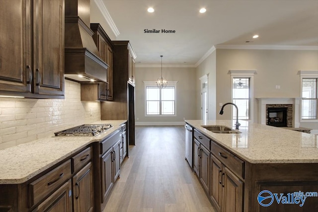 kitchen featuring appliances with stainless steel finishes, sink, custom exhaust hood, light stone counters, and a center island with sink