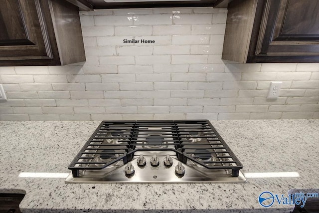 interior details with dark brown cabinetry, light stone countertops, stainless steel gas cooktop, and decorative backsplash