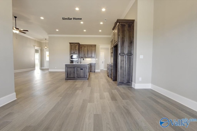 kitchen with stainless steel microwave, crown molding, light hardwood / wood-style floors, and an island with sink