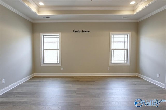 empty room featuring wood-type flooring, crown molding, and a tray ceiling