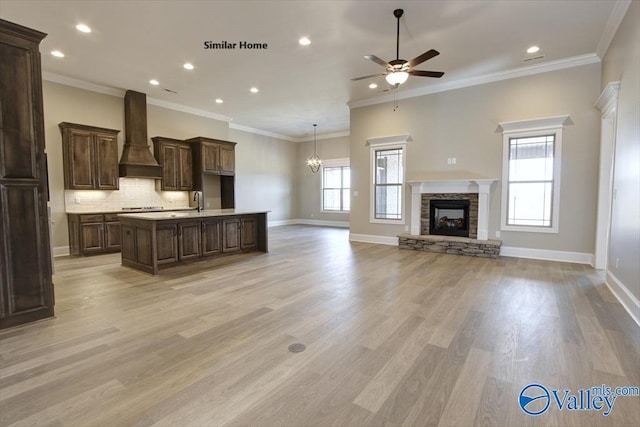 kitchen with a healthy amount of sunlight, a stone fireplace, a kitchen island with sink, and custom exhaust hood