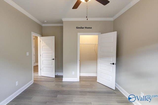 unfurnished bedroom featuring crown molding, a spacious closet, ceiling fan, and light hardwood / wood-style flooring