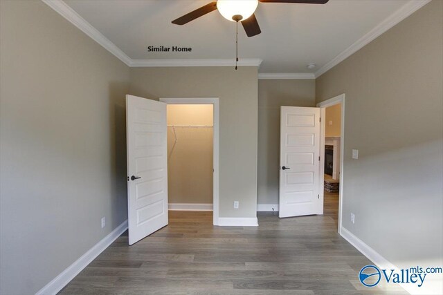 unfurnished bedroom with hardwood / wood-style flooring, crown molding, a walk in closet, and ceiling fan