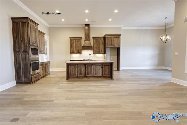 kitchen with sink, premium range hood, an island with sink, built in microwave, and oven