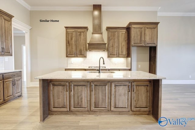 kitchen featuring custom exhaust hood, an island with sink, sink, and light stone counters