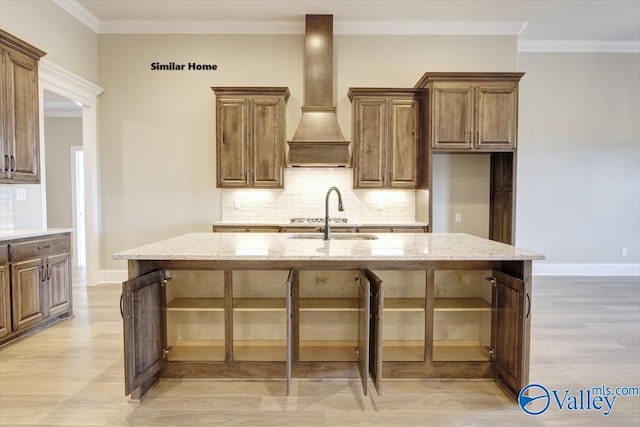 kitchen with sink, light stone countertops, premium range hood, and a center island with sink