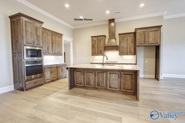 kitchen featuring built in microwave, custom exhaust hood, a kitchen island with sink, stainless steel oven, and crown molding