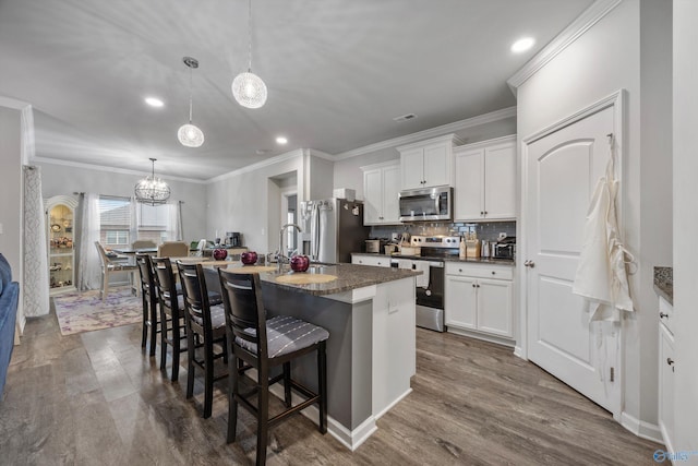 kitchen with appliances with stainless steel finishes, decorative light fixtures, white cabinetry, a kitchen bar, and a center island with sink