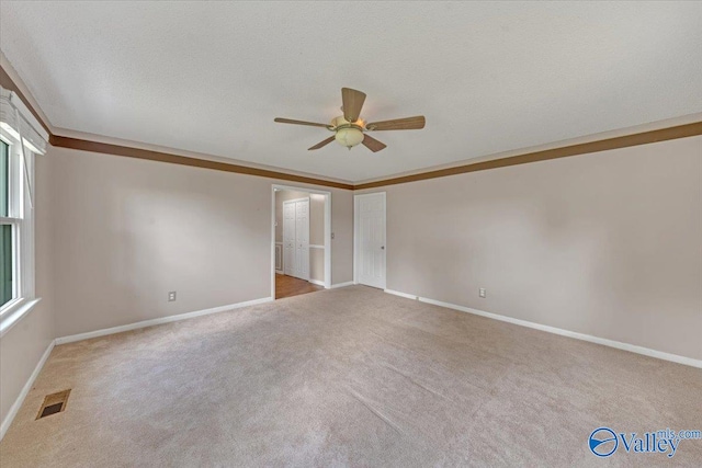 empty room featuring light carpet, crown molding, a textured ceiling, and ceiling fan