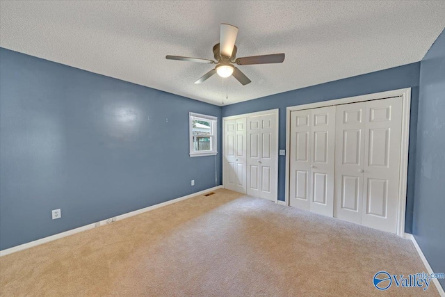 unfurnished bedroom with carpet flooring, ceiling fan, multiple closets, and a textured ceiling