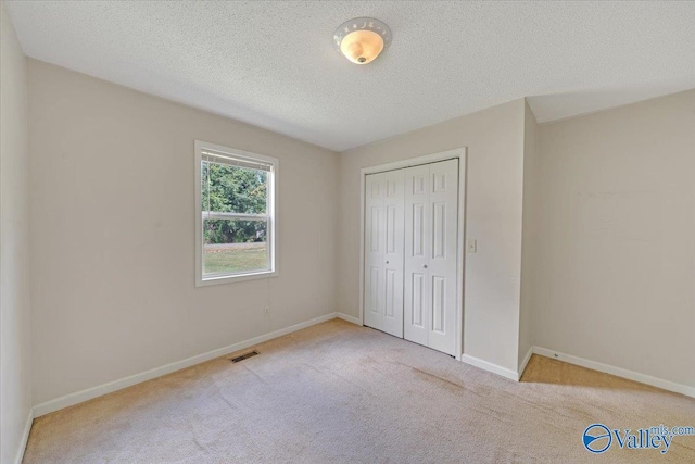 unfurnished bedroom featuring baseboards, visible vents, a textured ceiling, carpet flooring, and a closet