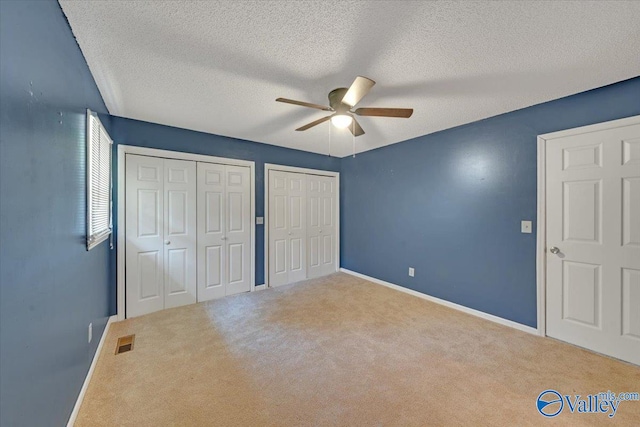 unfurnished bedroom with a textured ceiling, carpet flooring, ceiling fan, and multiple closets