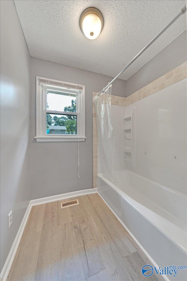 bathroom featuring shower / bath combination with curtain, wood-type flooring, and a textured ceiling