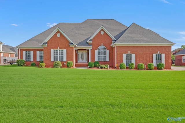 view of front of house with a front yard, brick siding, and roof with shingles