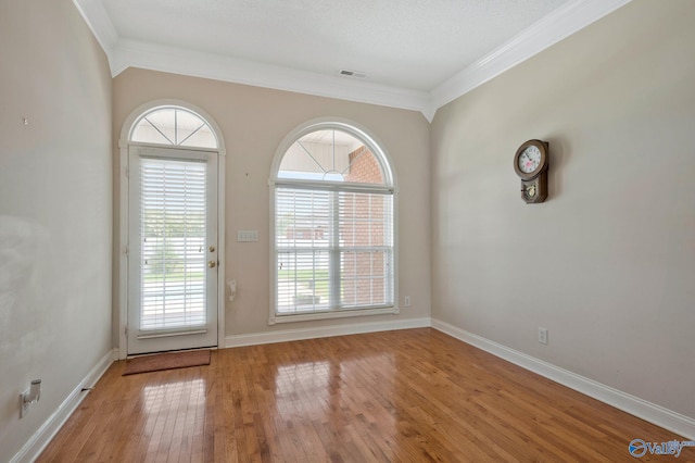 doorway with ornamental molding, visible vents, baseboards, and wood finished floors