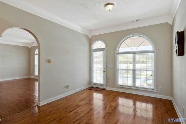 entrance foyer with hardwood / wood-style flooring, visible vents, arched walkways, and ornamental molding